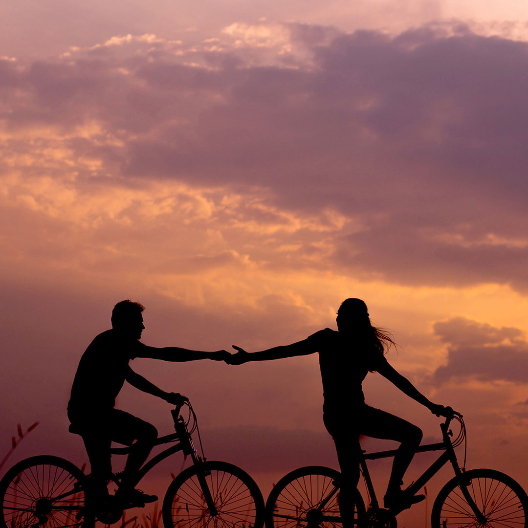 Silhouette of two bicycle riders against a dusky sky