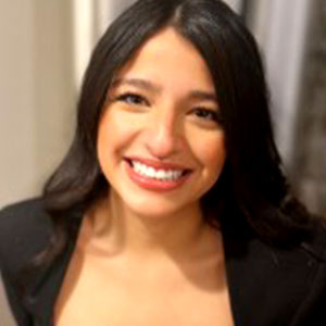 Rhuby Ocampo has long brown hair, white skin, and a wide smile. She is wearing a black jacket.