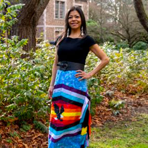 Emma Elliott stands with her left hand on her hip. She wears a long skirt patterned with vivid stripes and an eagle.