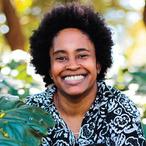 Jarre Hamilton smiles broadly. She has dark brown skin and wears her hair in an afro. She is wearing a black shirt with white patterns.