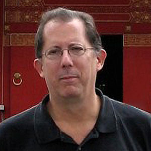 Tracy Collier is a caucasian male, with short brown hair and wire-rimmed glasses. He is smiling faintly and wears a casual black polo shirt.