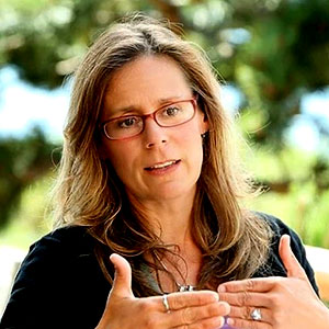 Dr. Deborah Giles is a white woman with long sandy brown hair. She wears glasses and holds her hands in front of her.