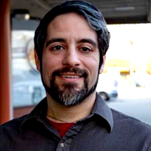 Dan Tucker is a white male with dark hair and beard. He smiles and wears a dark gray shirt.