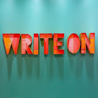 Art installation on a mint green background with giant red and orange textured block letters that read write on