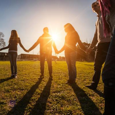 Group of people holding hands in a circle outside in the sunshine