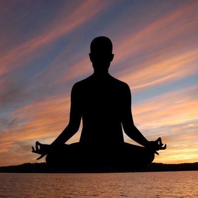 Silhouette of figure in seated yoga pose against a dusky sky