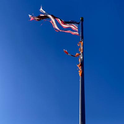Flagpole with fluttering and tattered Unites States flag against a bright blue sky