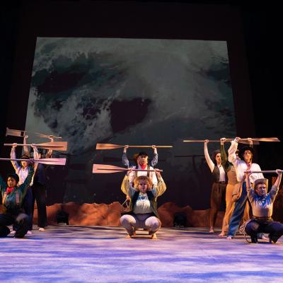 Group of WWU theatre students on stage holding wooden oars above their heads