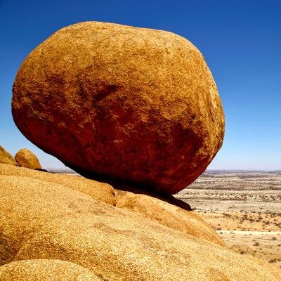 Giant boulder perched on the edge of a bluff overlooking a desert landscape