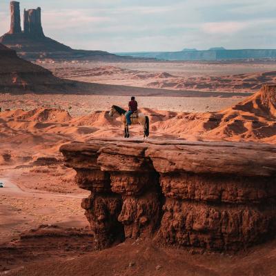Lone horseman on a rocky bluff overlooking dramatic vista of Monument Valley in Arizona