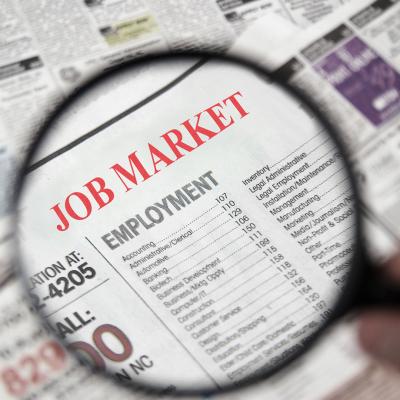 Magnifying glass above a newspaper headline reading job market and employment
