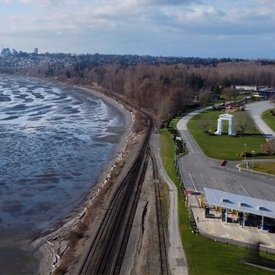 Sweeping view of US/Canada border crossing at Blaine, Washington with rippling water, train tracks, trees, green grass, and the Peace Arch monument.