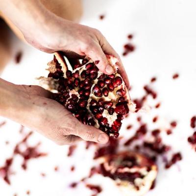 Close up of a woman's hands holding a broken open pomegranate with blood red juice on a white floor.
