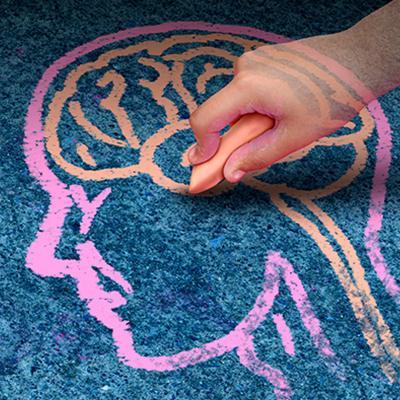 A child's hand holds a large piece of orange chalk and draws the outline of a human brain.