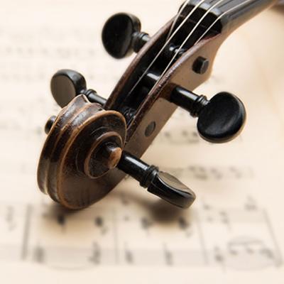 The scroll of an old violin with black tuning pegs rests on sheet music.