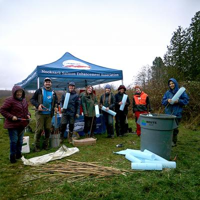 A group of WWU students gather outside with tools and supplies by a Nooksack Salmon Enhancement Association tent.