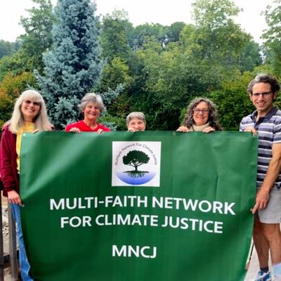 Members of the Multi-Faith Network for Climate Justice proudly hold a large green banner for their organization.