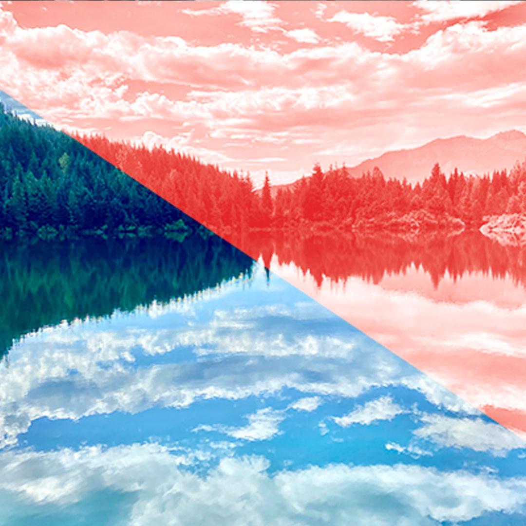 Blue sky and clouds are reflected on the surface of a lake with a forest in the background.