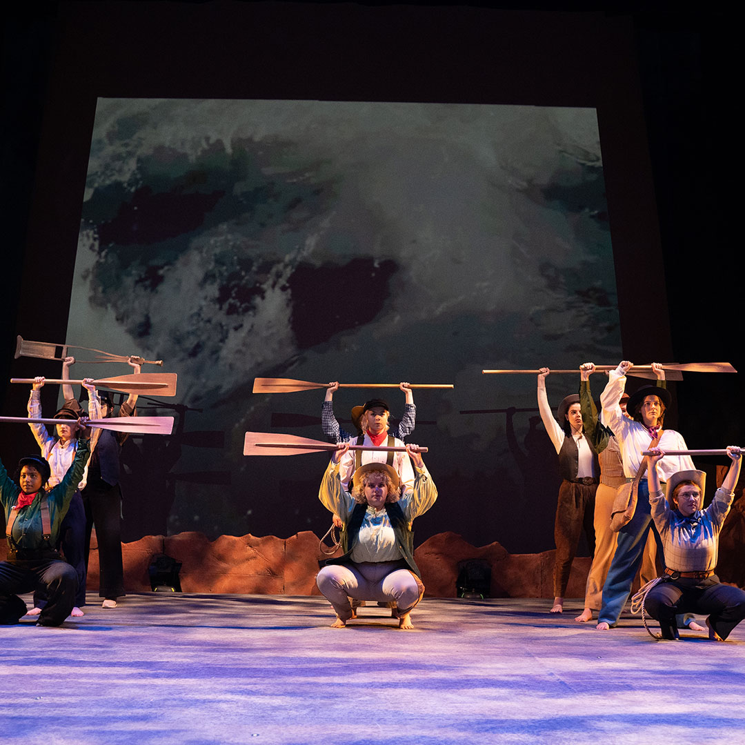 Group of WWU theatre students on stage holding wooden oars above their heads