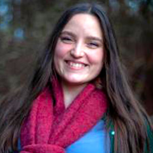 Alexi Guddal is a white woman with long brown hair. She smiles warmly and wears a red winter scarf and blue shirt.